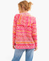 A woman shown from the back wearing a bright pink hooded long-sleeve top with an orange and white geometric pattern, paired with blue jeans, against a plain white background.