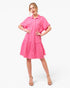 A woman modeling a bright pink short-sleeve tiered shirt dress with a button-front design and chest pockets, paired with beige heeled sandals, against a plain white studio background.