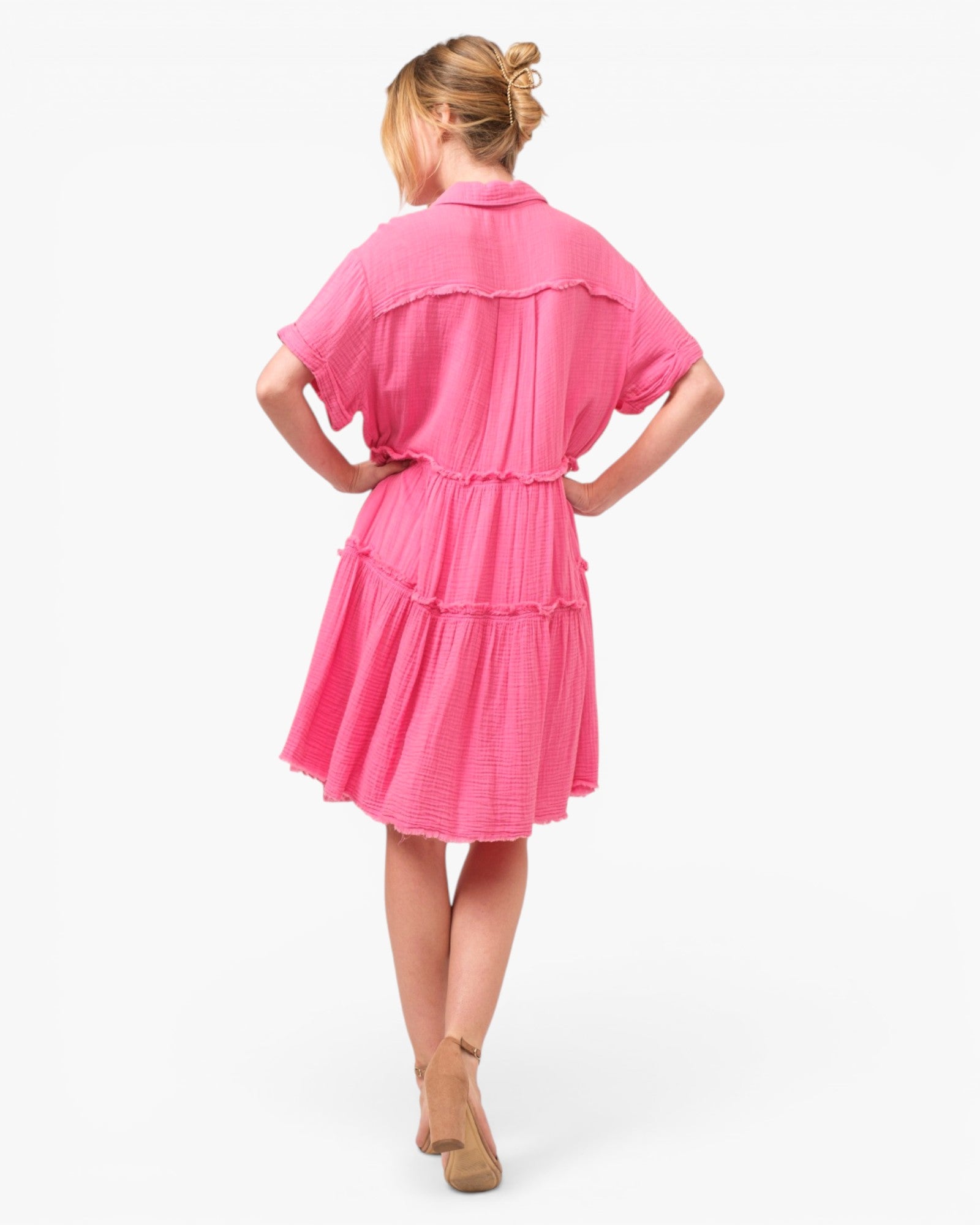 A woman wearing a bright pink tiered short-sleeve dress, shown from the back against a plain white studio background.