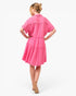 A woman wearing a bright pink tiered short-sleeve dress, shown from the back against a plain white studio background.