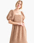 A woman wearing a textured, chunky knit midi dress in a warm tan color, featuring puff sleeves and a square neckline, set against a plain white background.