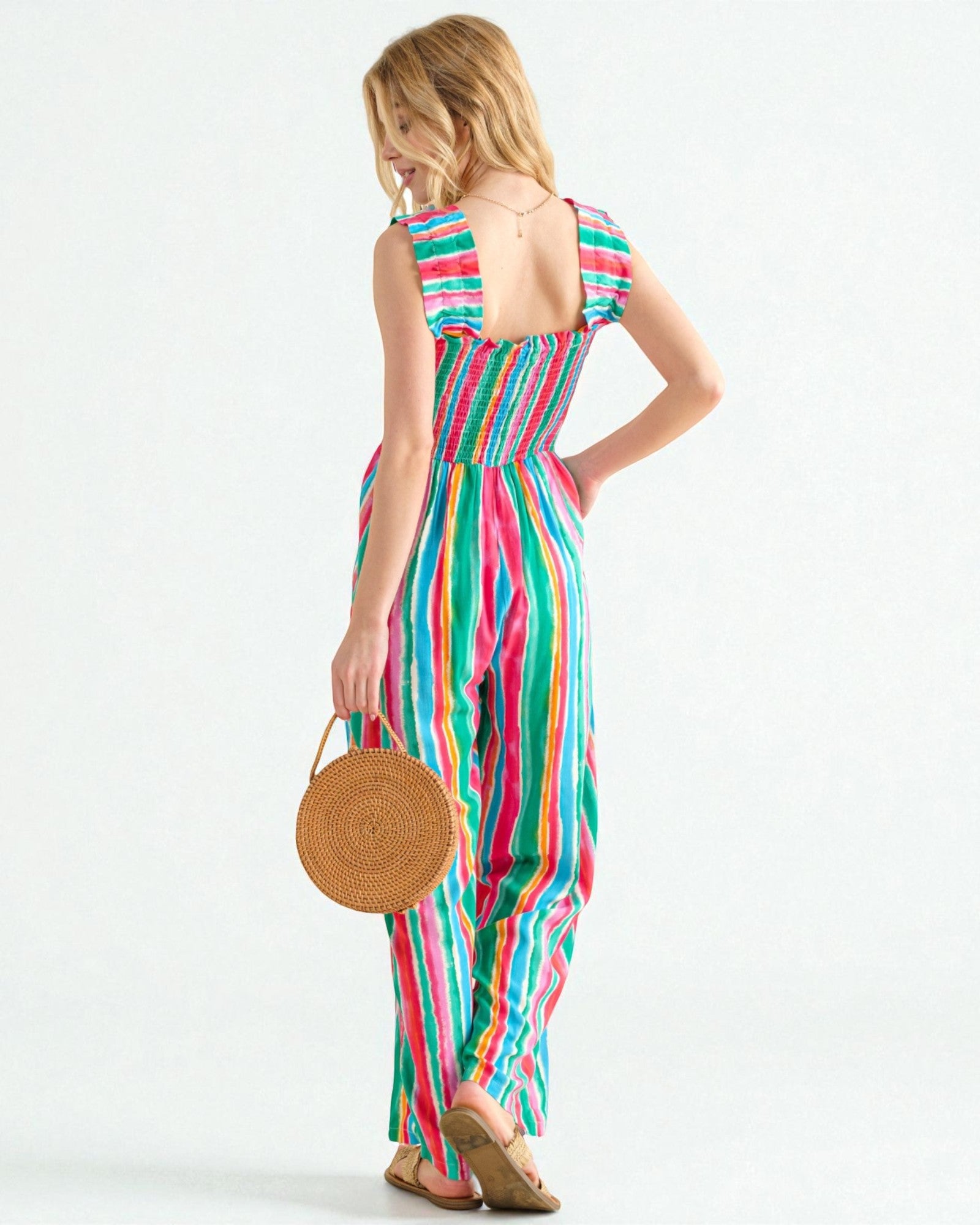 Woman wearing a colorful striped dress holding a woven bag on a white background