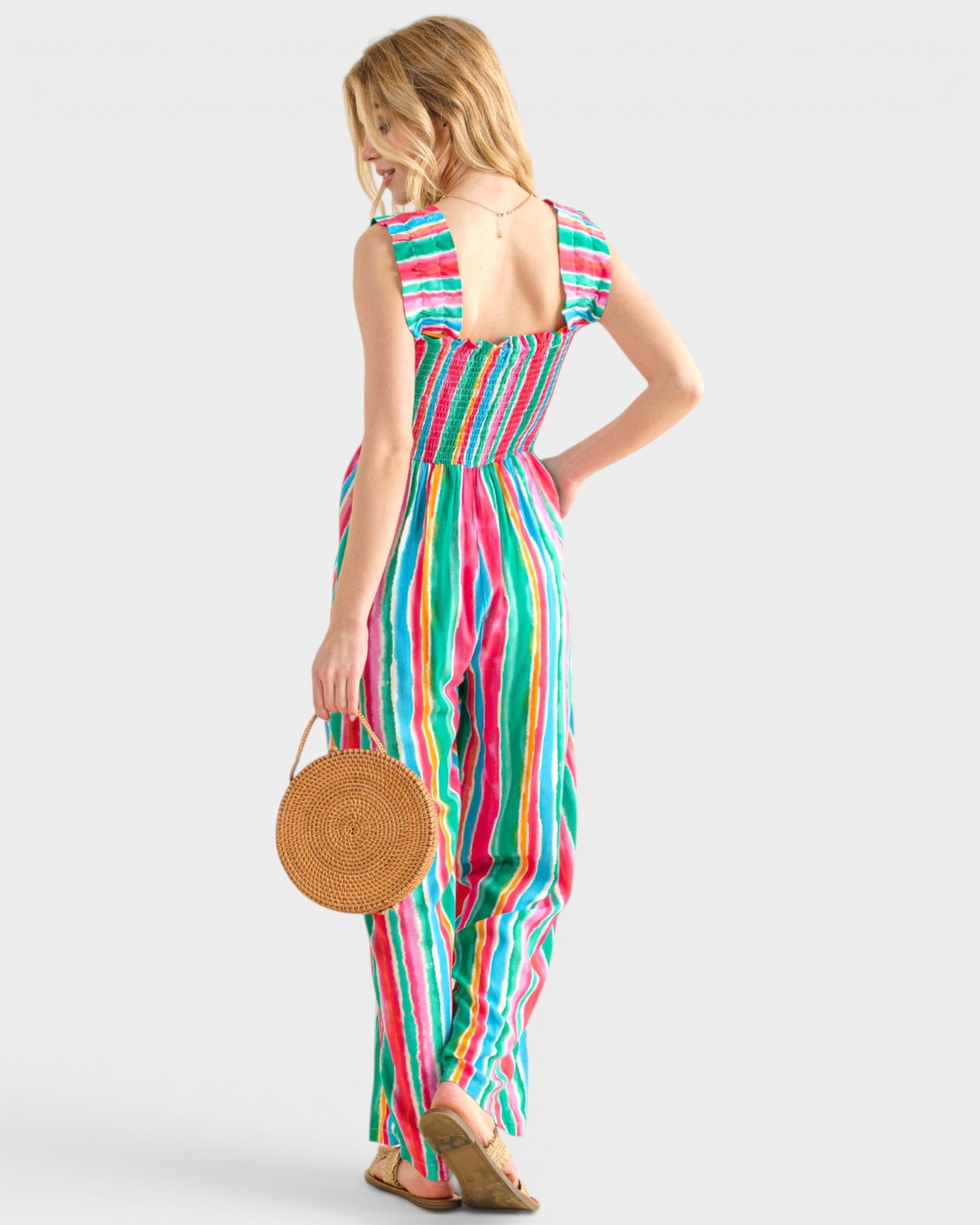 Woman wearing a colorful striped jumpsuit holding a round woven bag on a white background