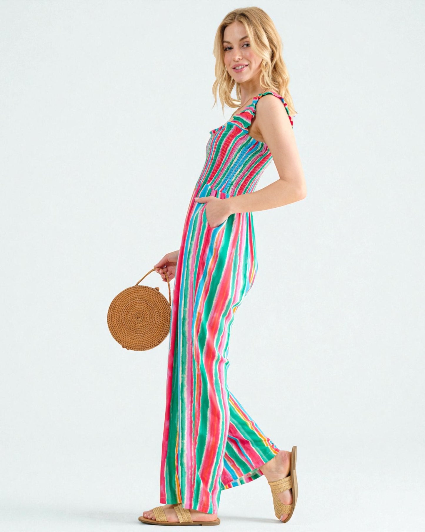 Woman wearing a colorful striped dress holding a woven bag on a white background