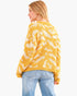 A woman shown from the back wearing a yellow and cream textured knit sweater and light blue jeans against a plain white background.