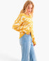 A woman wearing a chunky knit yellow and white patterned sweater with light blue jeans, photographed against a plain white studio background.