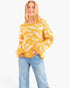 A woman wearing a yellow and cream wavy knit sweater with light blue jeans, standing against a plain white background.