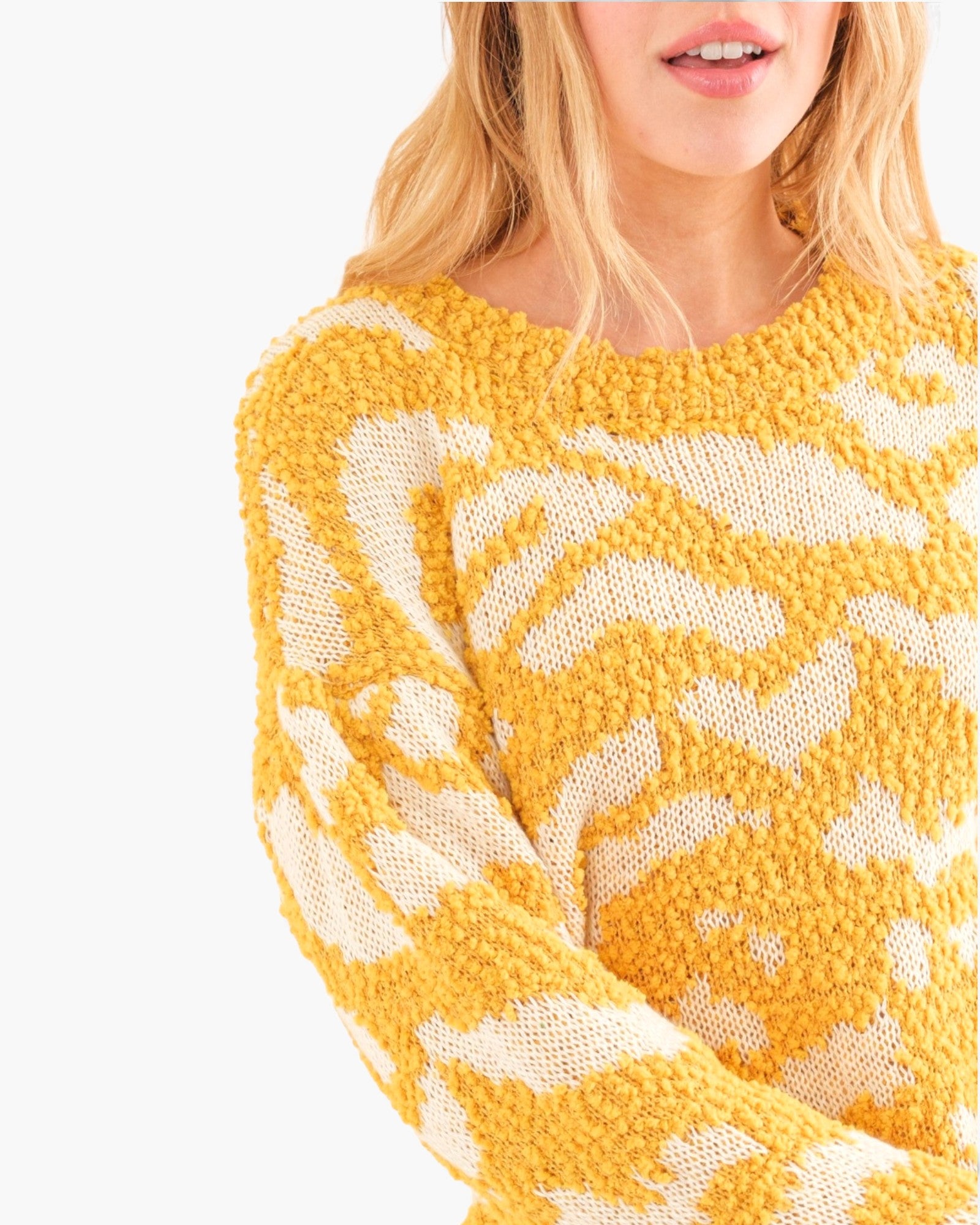 Close-up of a woman wearing a chunky knit sweater with a bold yellow and off-white abstract pattern, shown against a plain white background.