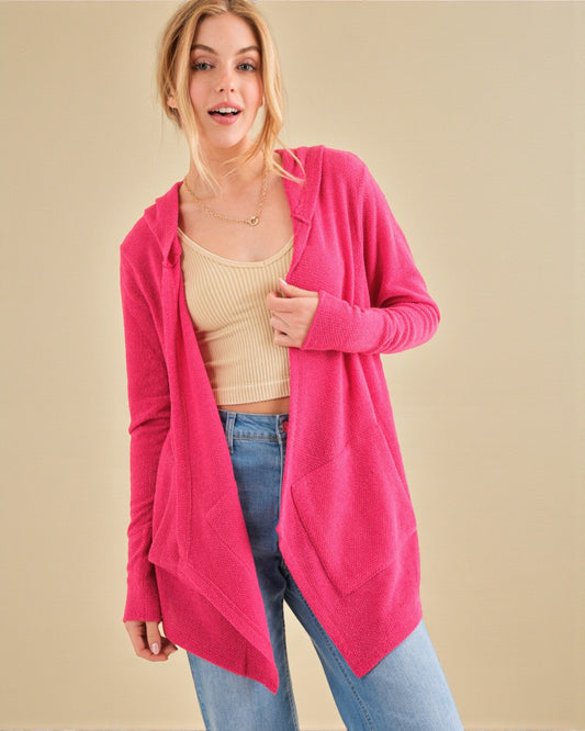 Woman wearing a bright pink cardigan over a beige top and blue jeans on a beige background