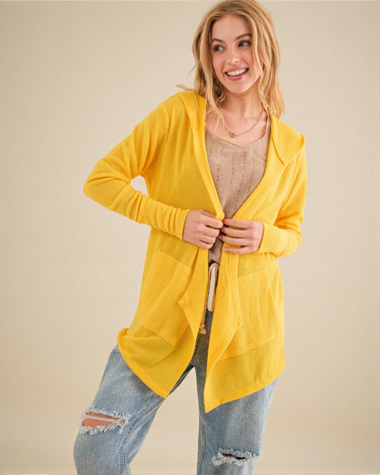 Woman wearing a yellow cardigan over a beige top and jeans on a beige background