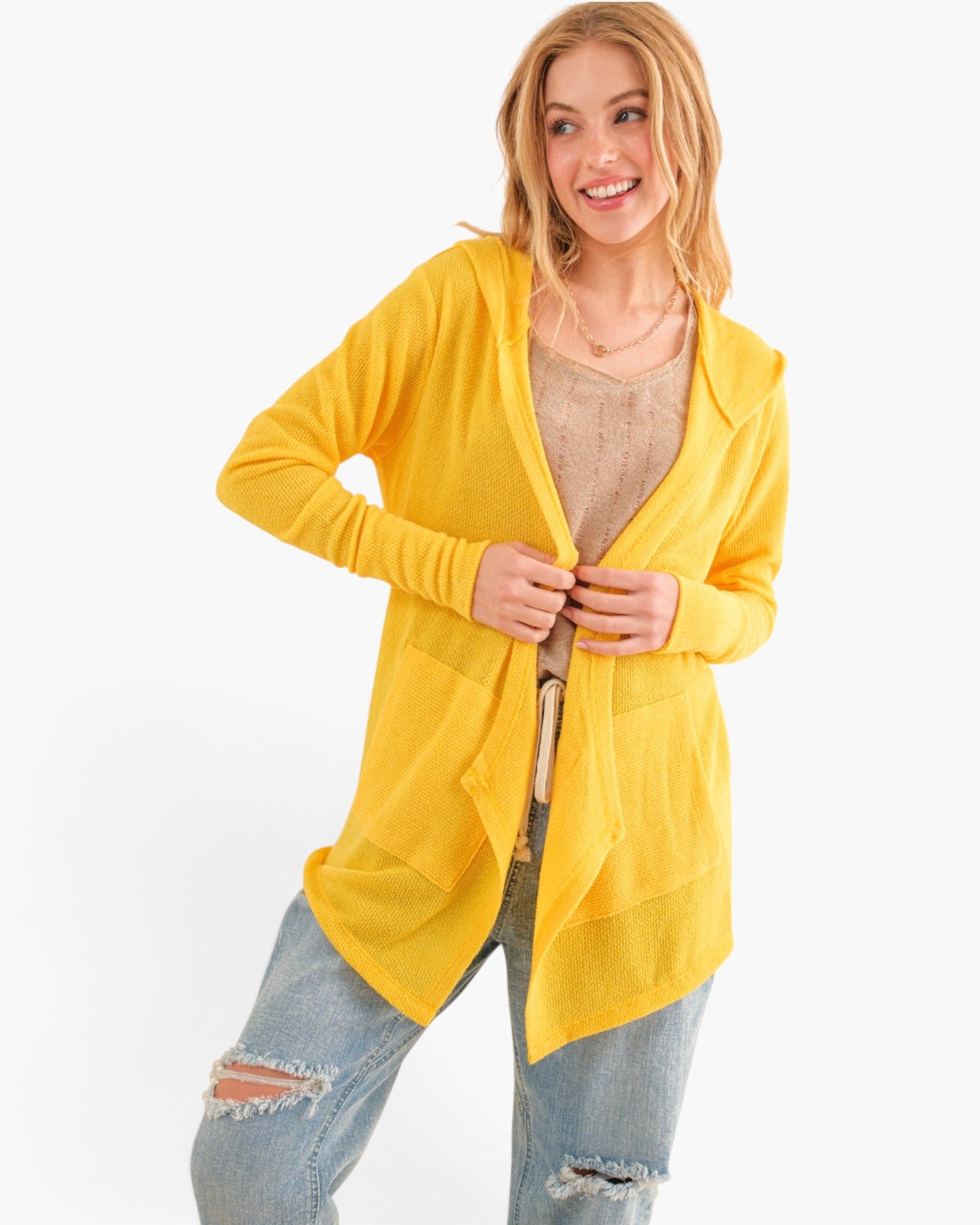 A woman modeling a bright yellow open-front cardigan over a beige top and distressed blue jeans, photographed against a clean white studio background.