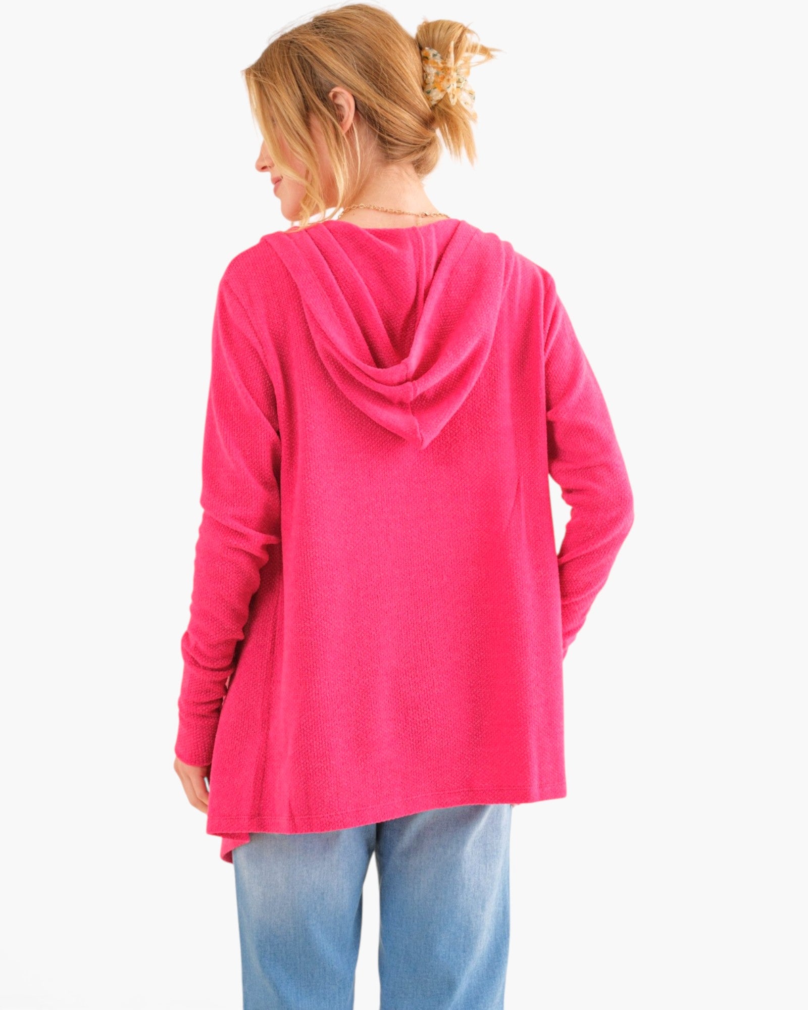 A woman shown from the back wearing a bright pink hooded long-sleeve top and light blue jeans against a plain white background.