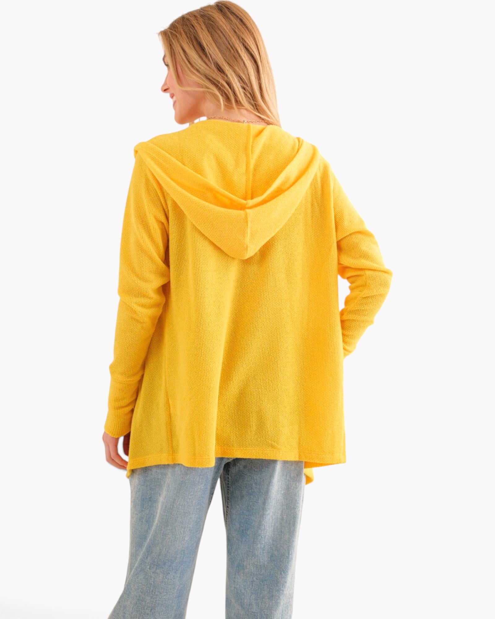A woman shown from the back wearing a bright yellow hooded sweatshirt and light blue jeans against a plain white studio background.