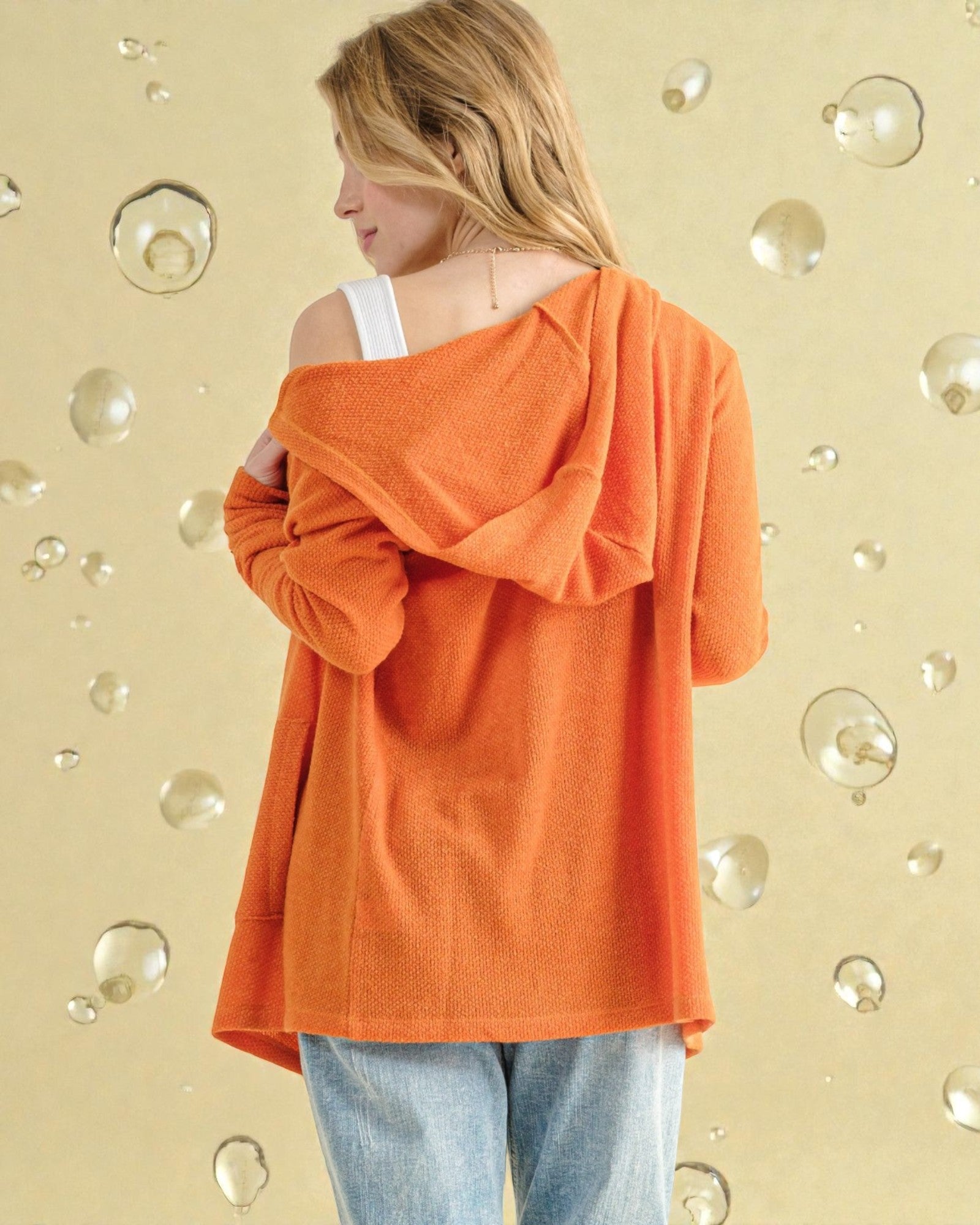 Person wearing an orange off-shoulder top against a bubble-patterned wall.