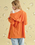 Person wearing an orange off-shoulder top against a bubble-patterned wall.