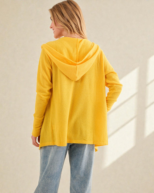 Person wearing a yellow hoodie and light blue jeans against a beige wall.