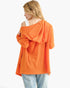 A woman shown from the back wearing a bright orange hooded pullover top with a draped hood, paired with light blue jeans, against a plain white background.