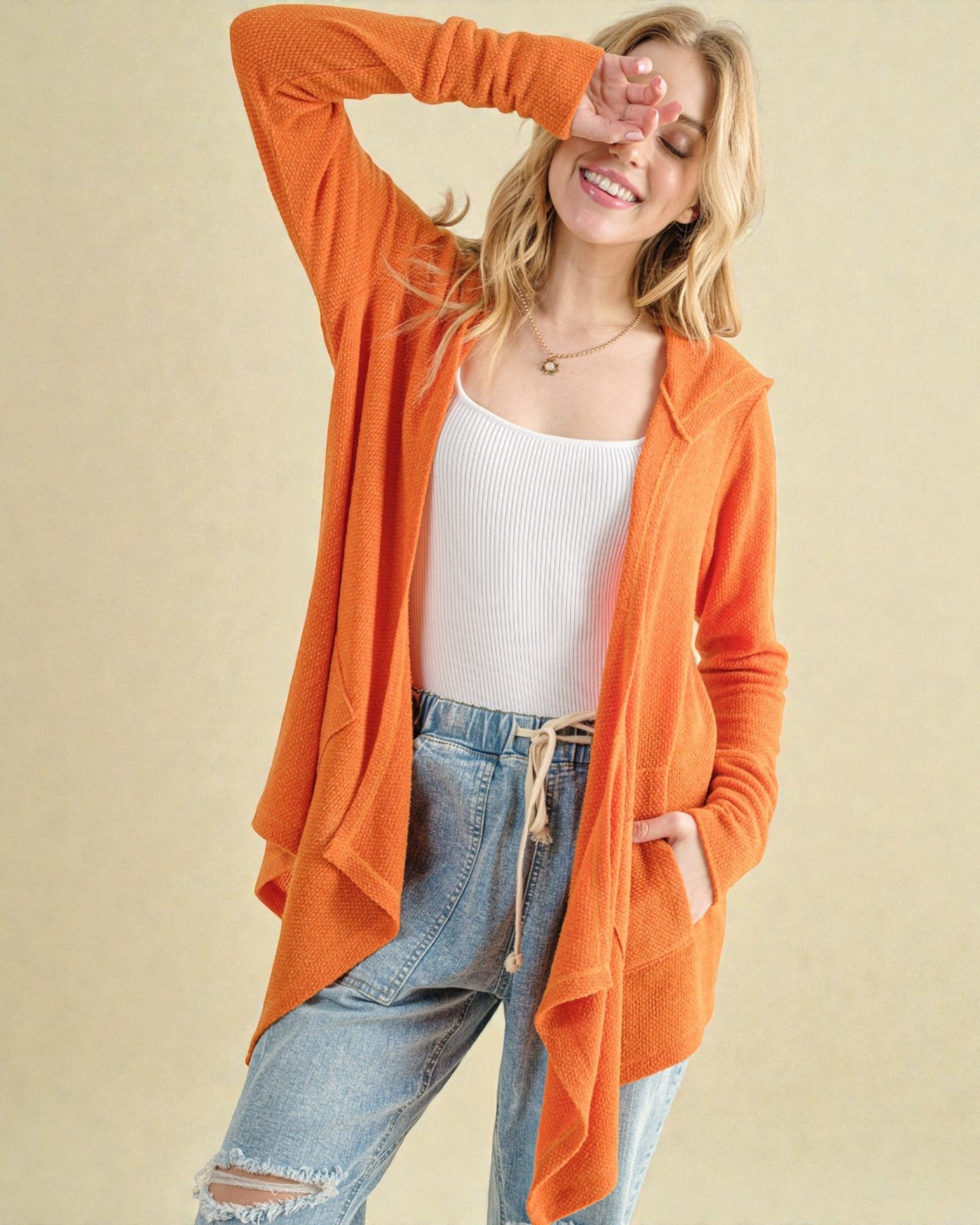 Woman wearing an orange cardigan over a white top and blue jeans on a beige background