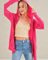 Woman wearing a bright pink hoodie, beige tank top, and blue jeans against a plain background