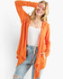 A woman modeling a bright orange open-front cardigan over a white ribbed tank top and light blue jeans, posed against a clean white studio background.
