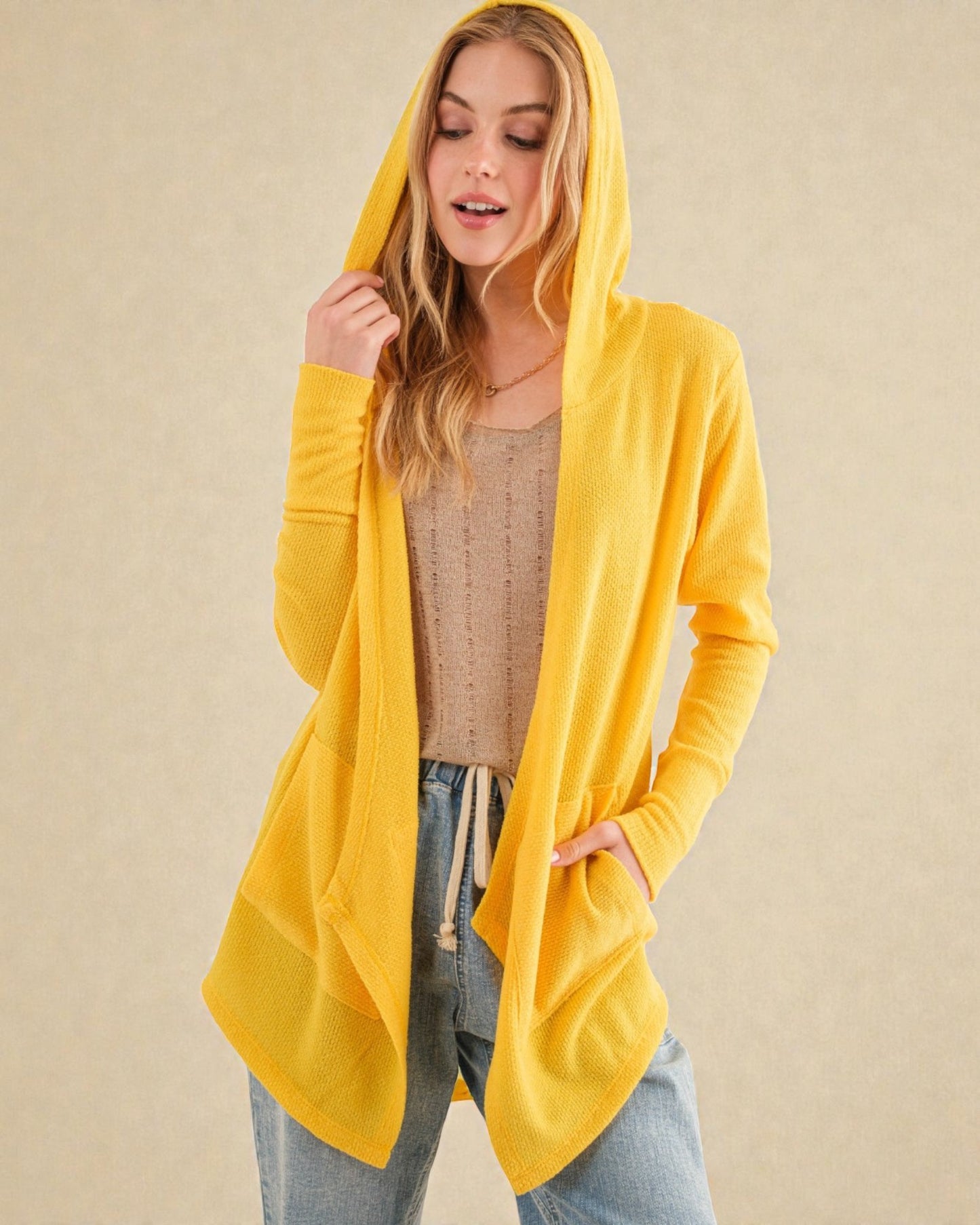 Woman wearing a yellow hooded cardigan on a beige background