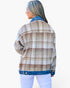 A woman shown from the back wearing a beige and brown plaid flannel jacket with a blue denim collar, hem, and cuffs, paired with white pants, against a plain white background.