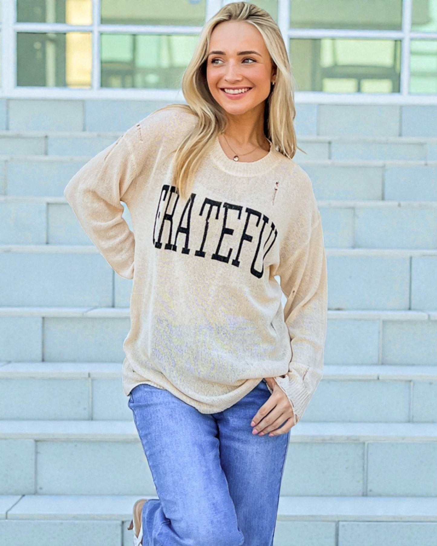 Woman wearing a beige sweater with 'GRATEFUL' text, standing on steps.