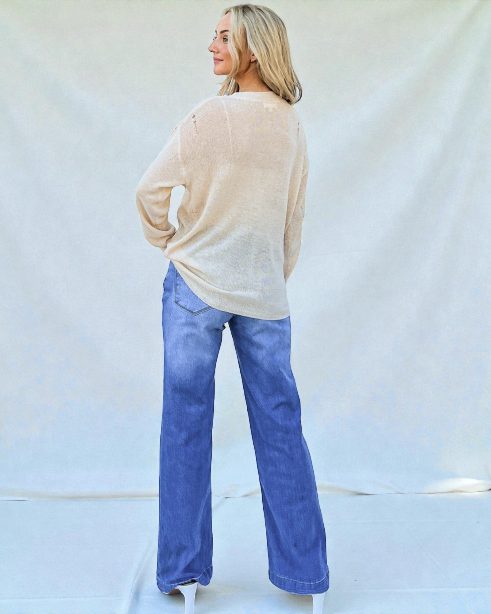 Woman wearing a beige sweater and blue jeans against a white background