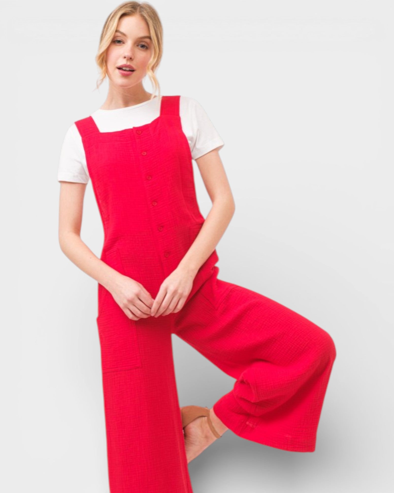 Woman wearing a red pinafore dress over a white shirt on a light gray background