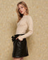 Woman wearing a beige sweater and black leather skirt against a beige background