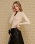 Woman wearing a beige sweater and black leather skirt against a textured beige wall.
