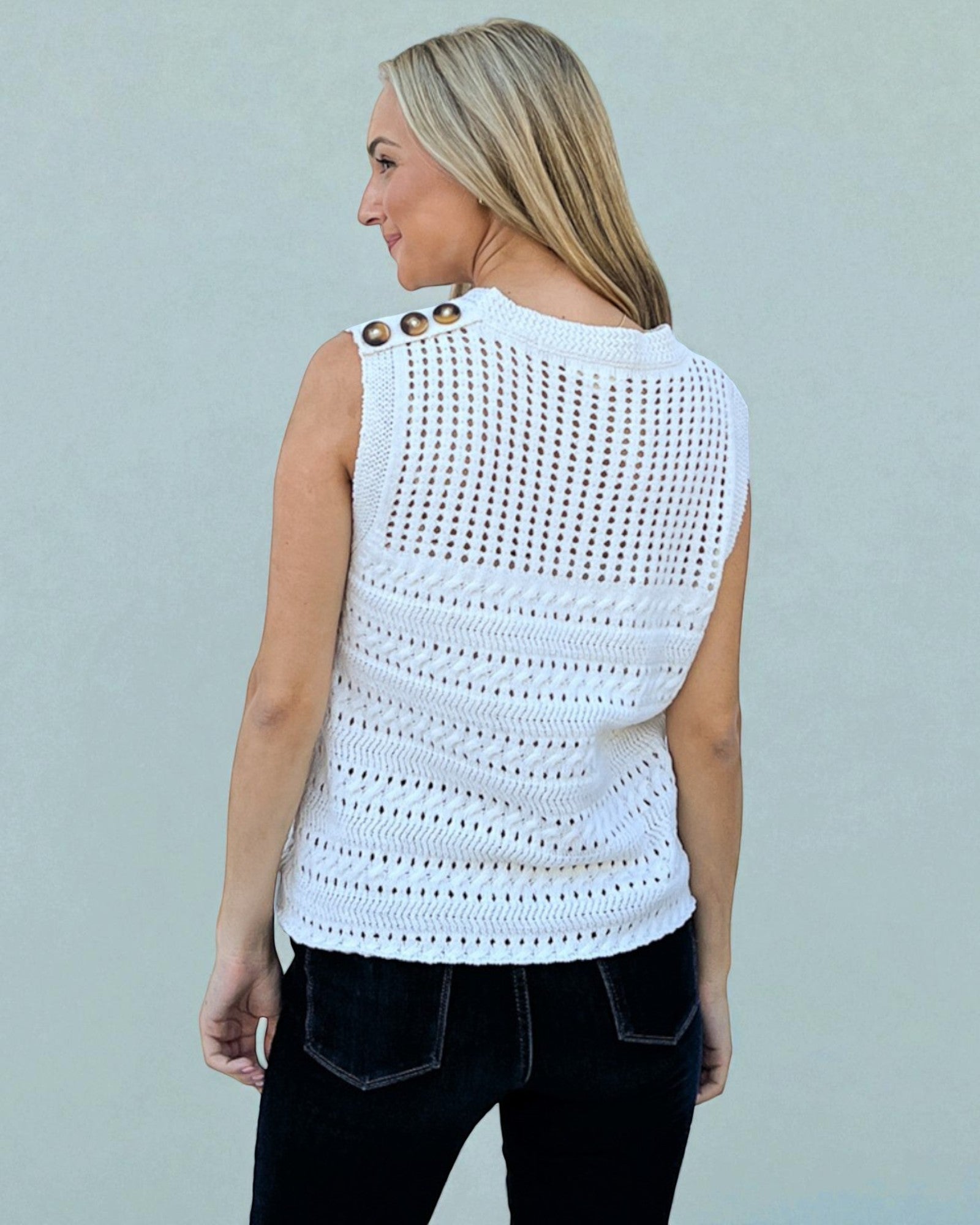 Woman wearing a white sleeveless crochet top against a light gray background