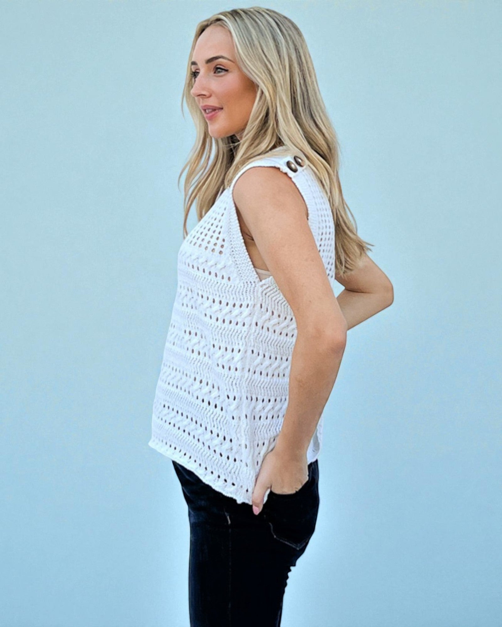 Woman wearing a white crochet sleeveless top against a light blue background