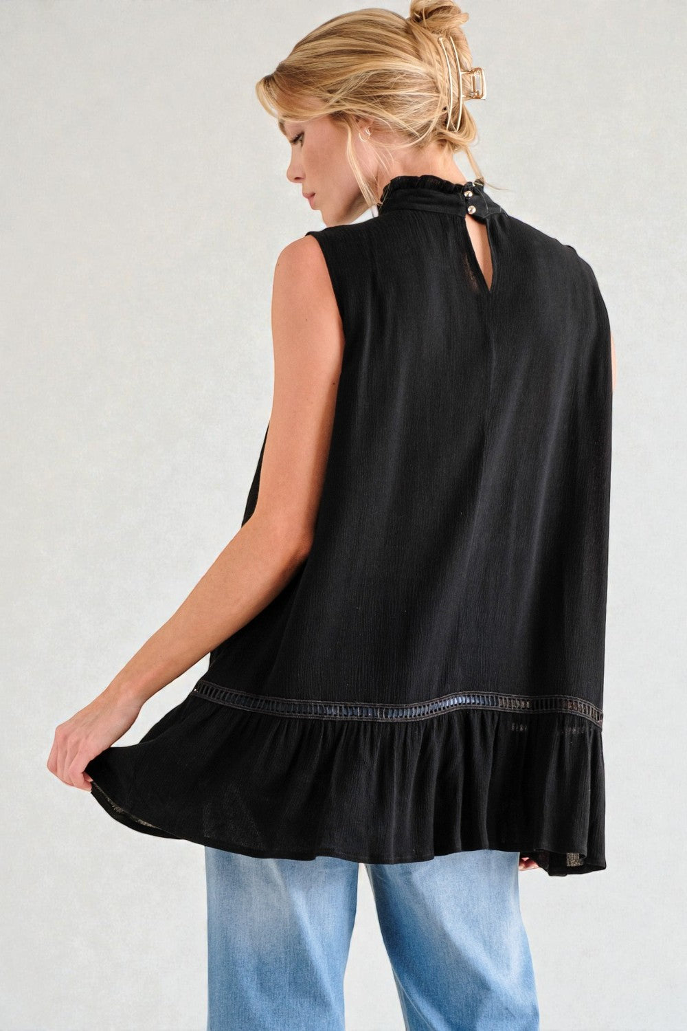 Woman wearing a black sleeveless top with a ruffled hem on a plain background
