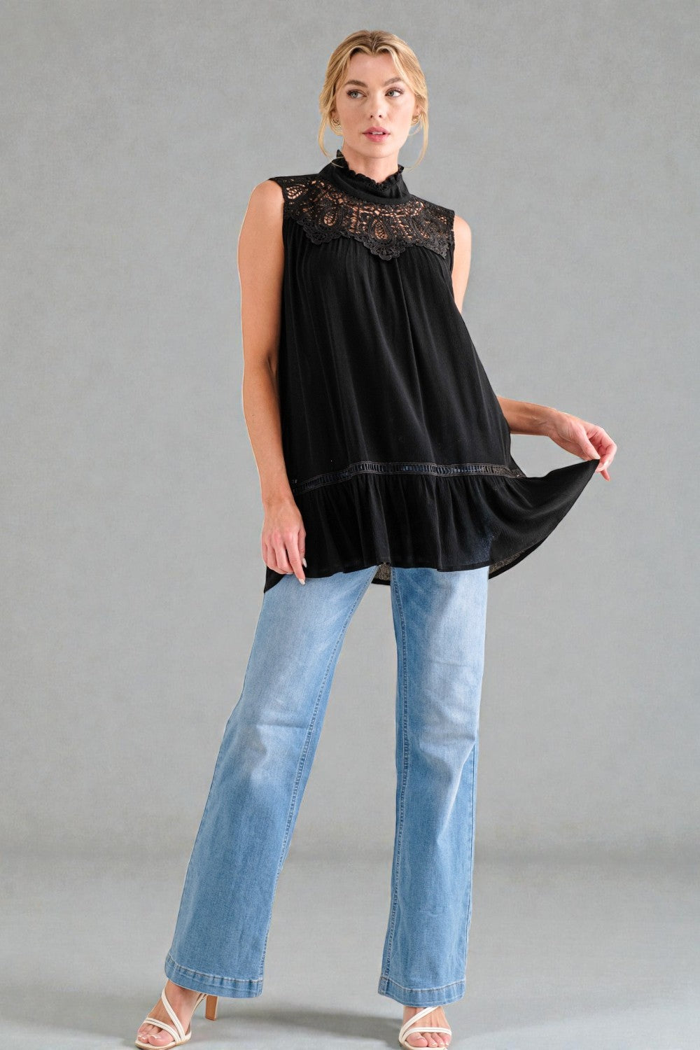Woman wearing a black sleeveless top with lace detail and blue jeans on a gray background