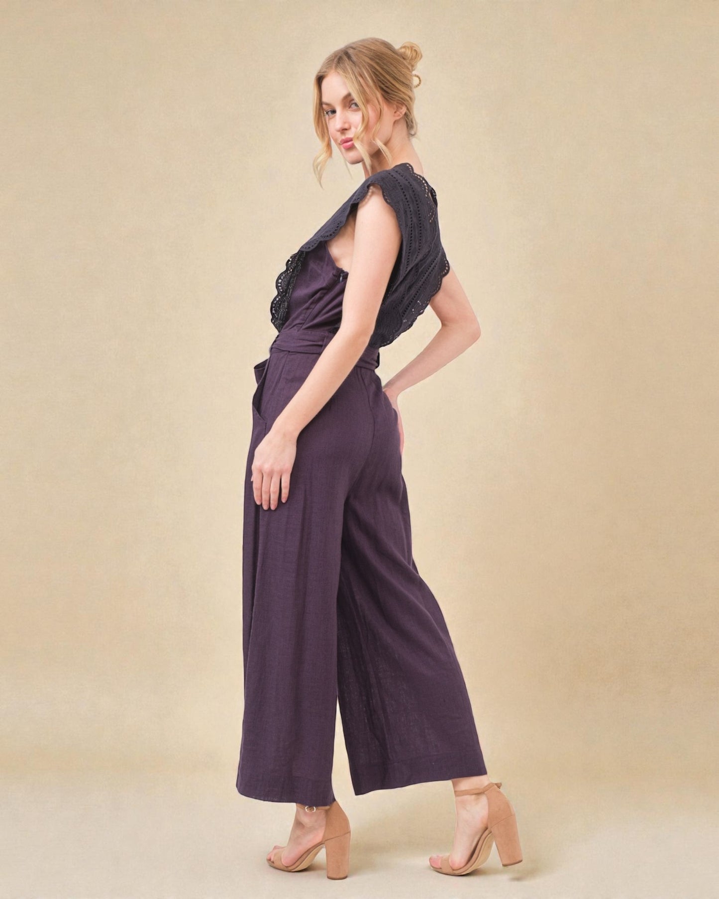 Woman wearing a dark purple jumpsuit on a beige background