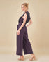 Woman wearing a dark purple jumpsuit on a beige background