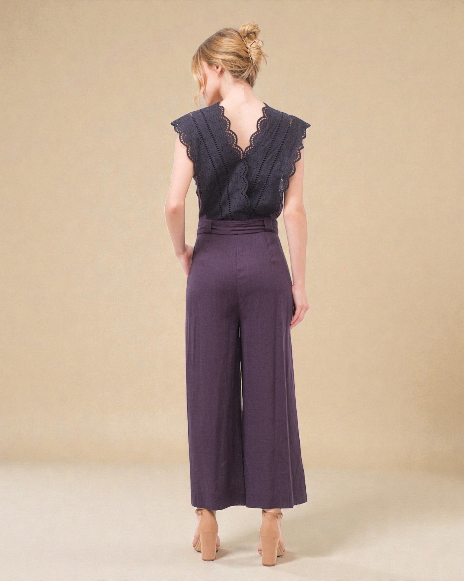 Woman wearing a dark purple jumpsuit with lace detailing on a beige background