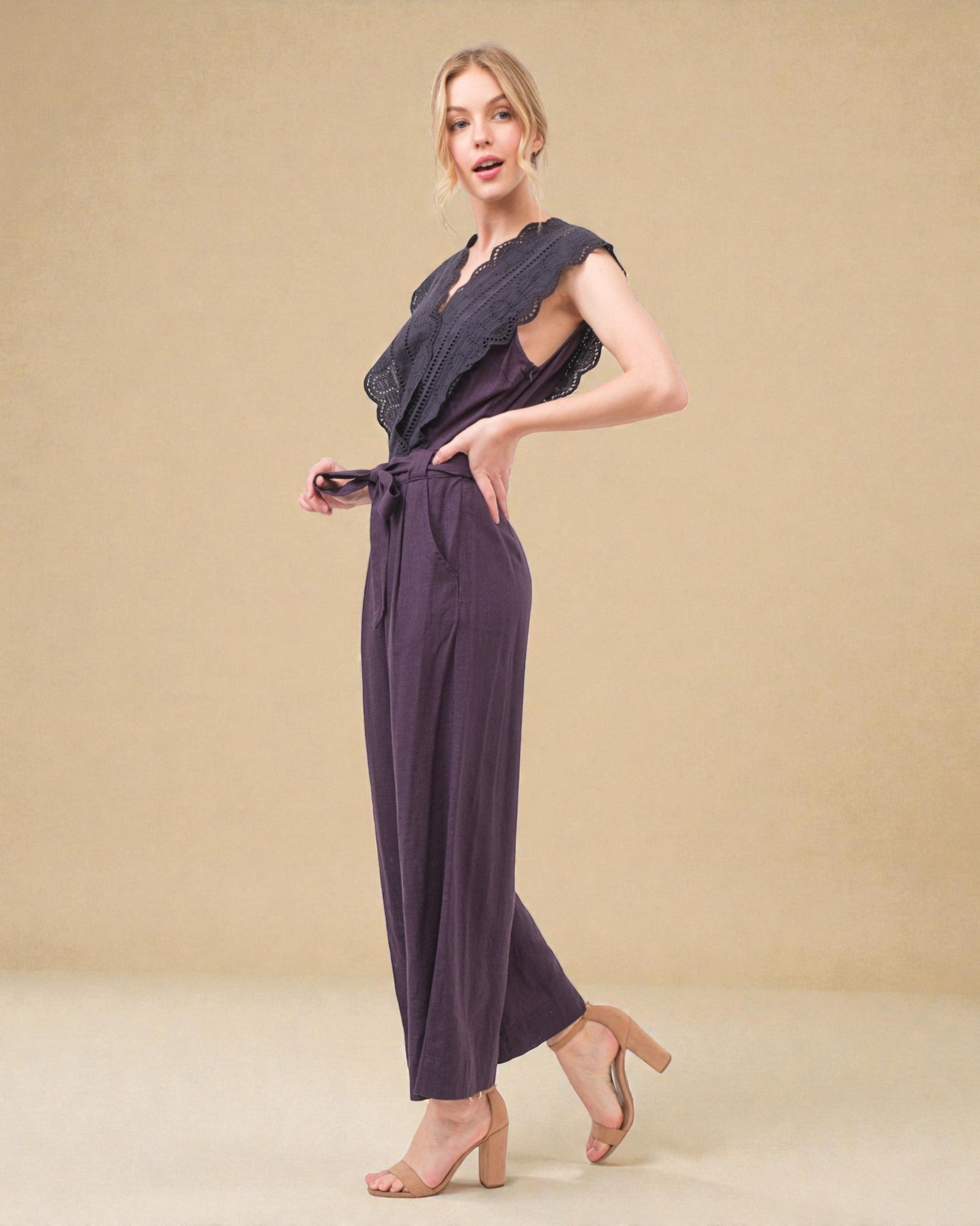 Woman wearing a dark purple jumpsuit with a textured top against a beige background