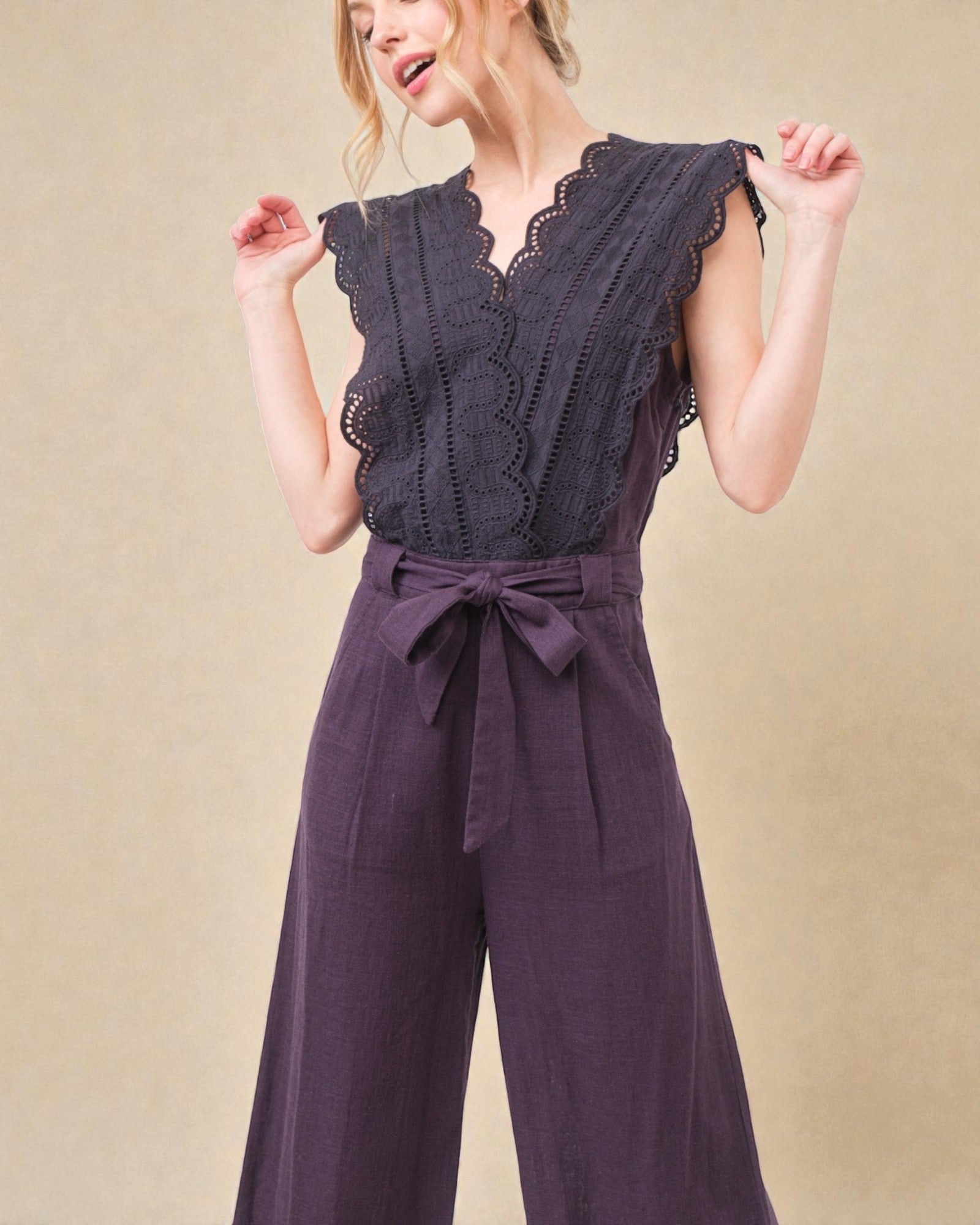 Woman wearing a dark purple jumpsuit with lace detailing on a beige background