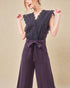 Woman wearing a dark purple jumpsuit with lace detailing on a beige background