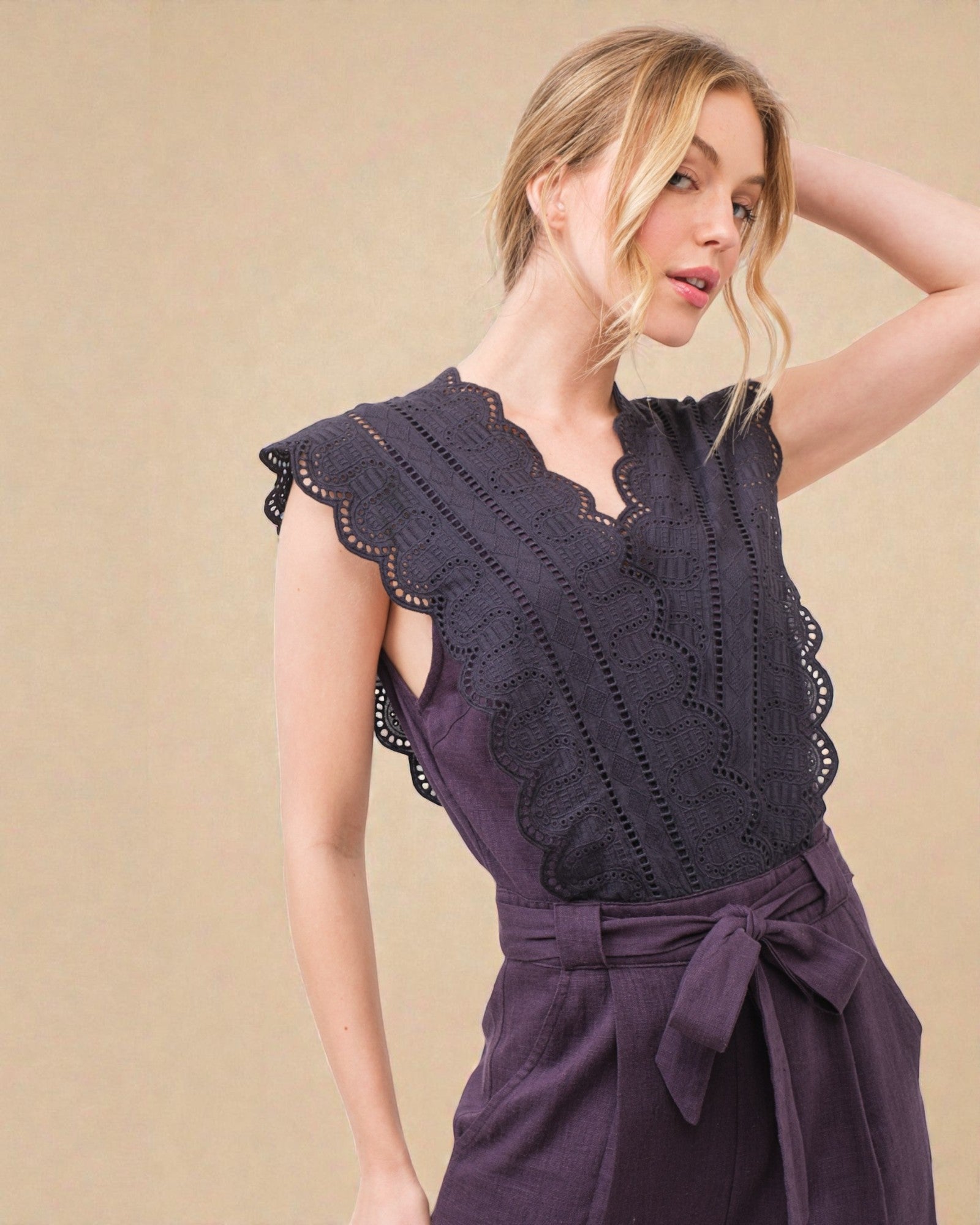 Woman wearing a dark purple top with lace details on a beige background