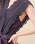 Close-up of a dark purple top with intricate cut-out details on a beige background