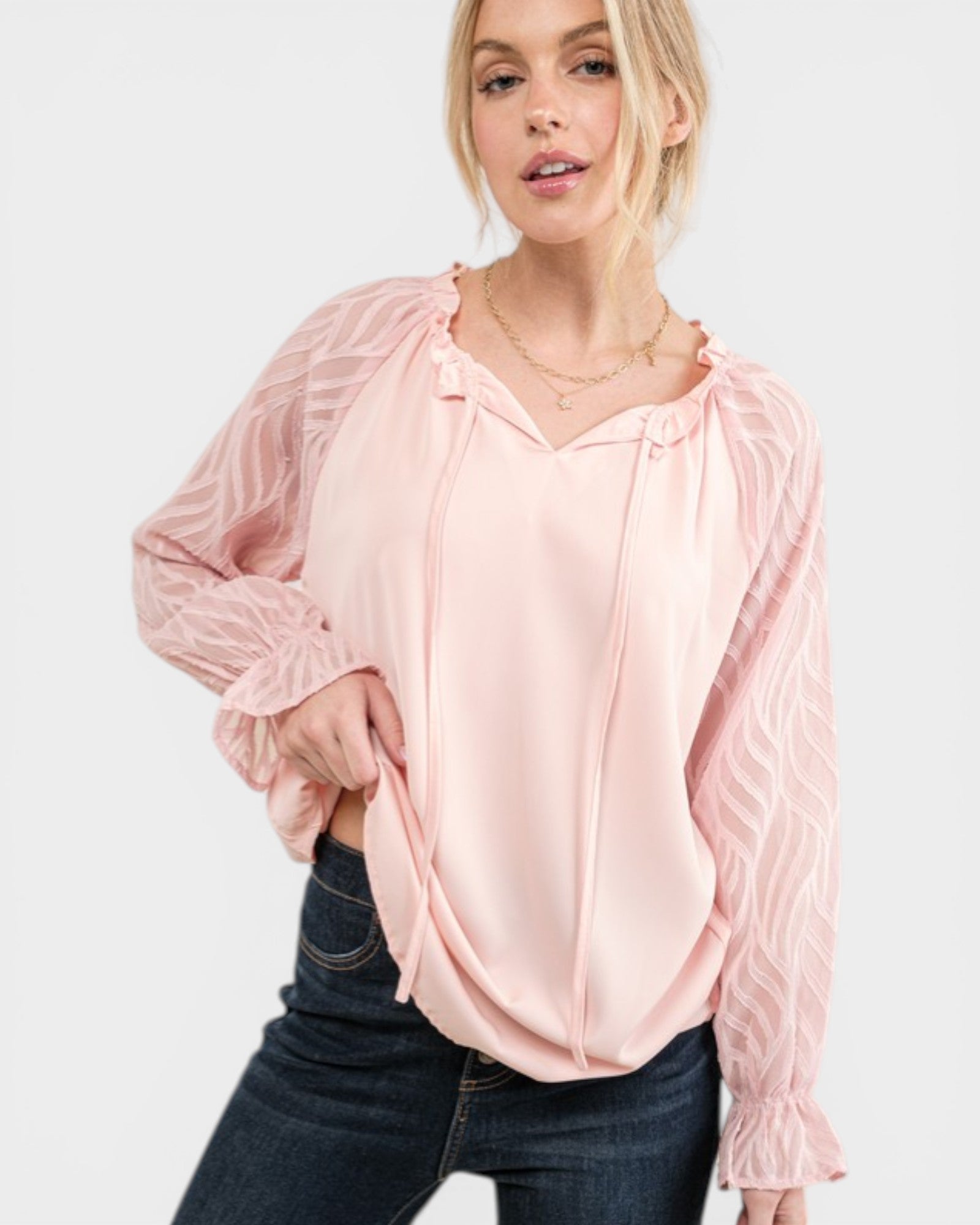 Woman wearing a light pink blouse with sheer sleeves on a white background