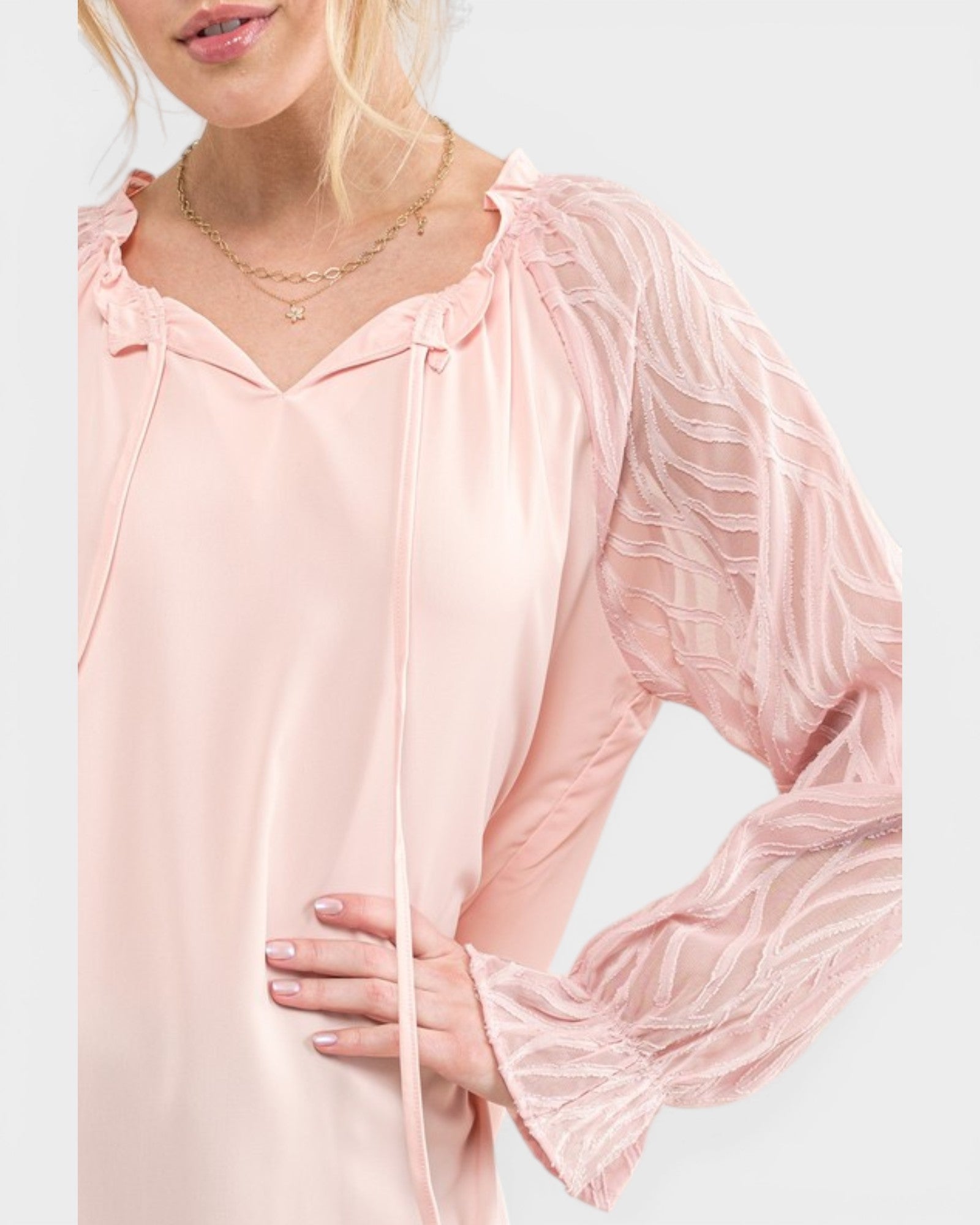 Woman wearing a light pink blouse with sheer sleeves on a white background