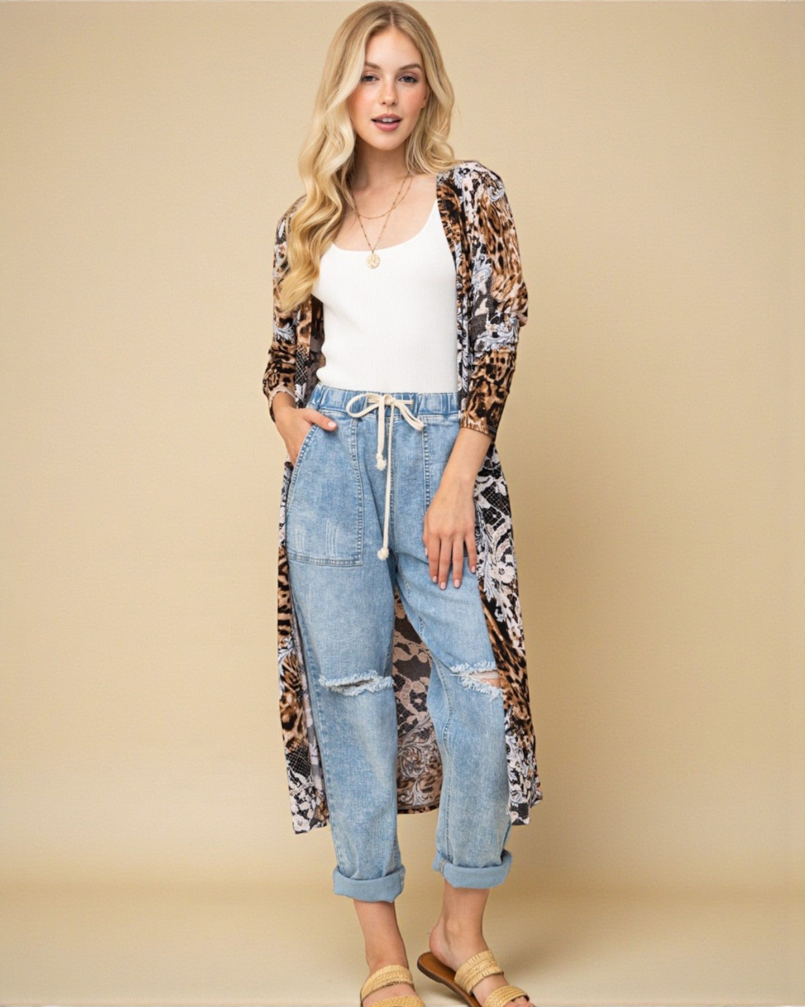 Woman wearing a long leopard print cardigan over a white top and jeans on a beige background