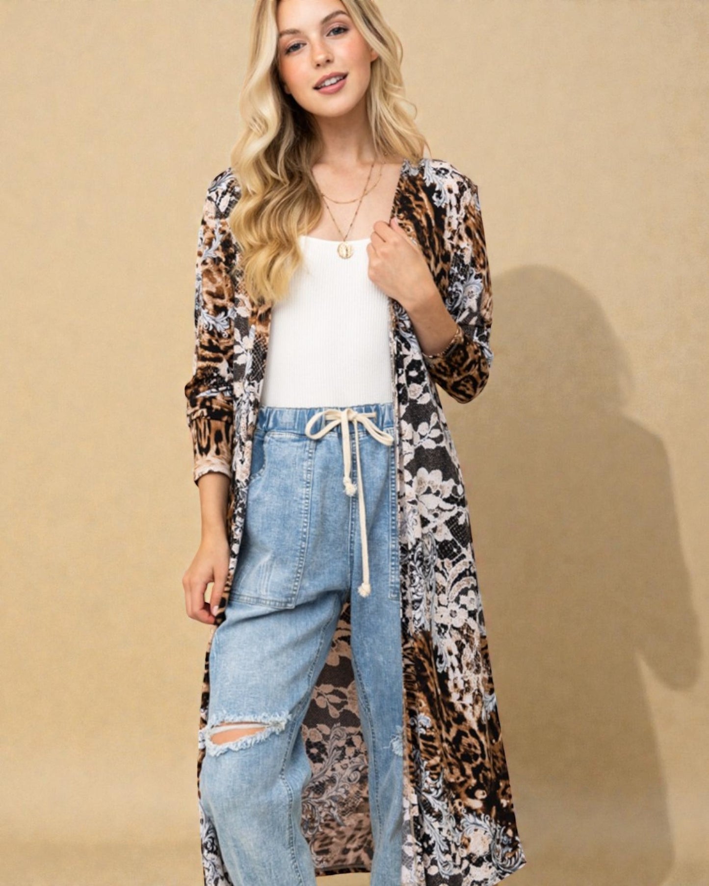 Woman wearing a long, patterned cardigan over a white top and jeans on a beige background
