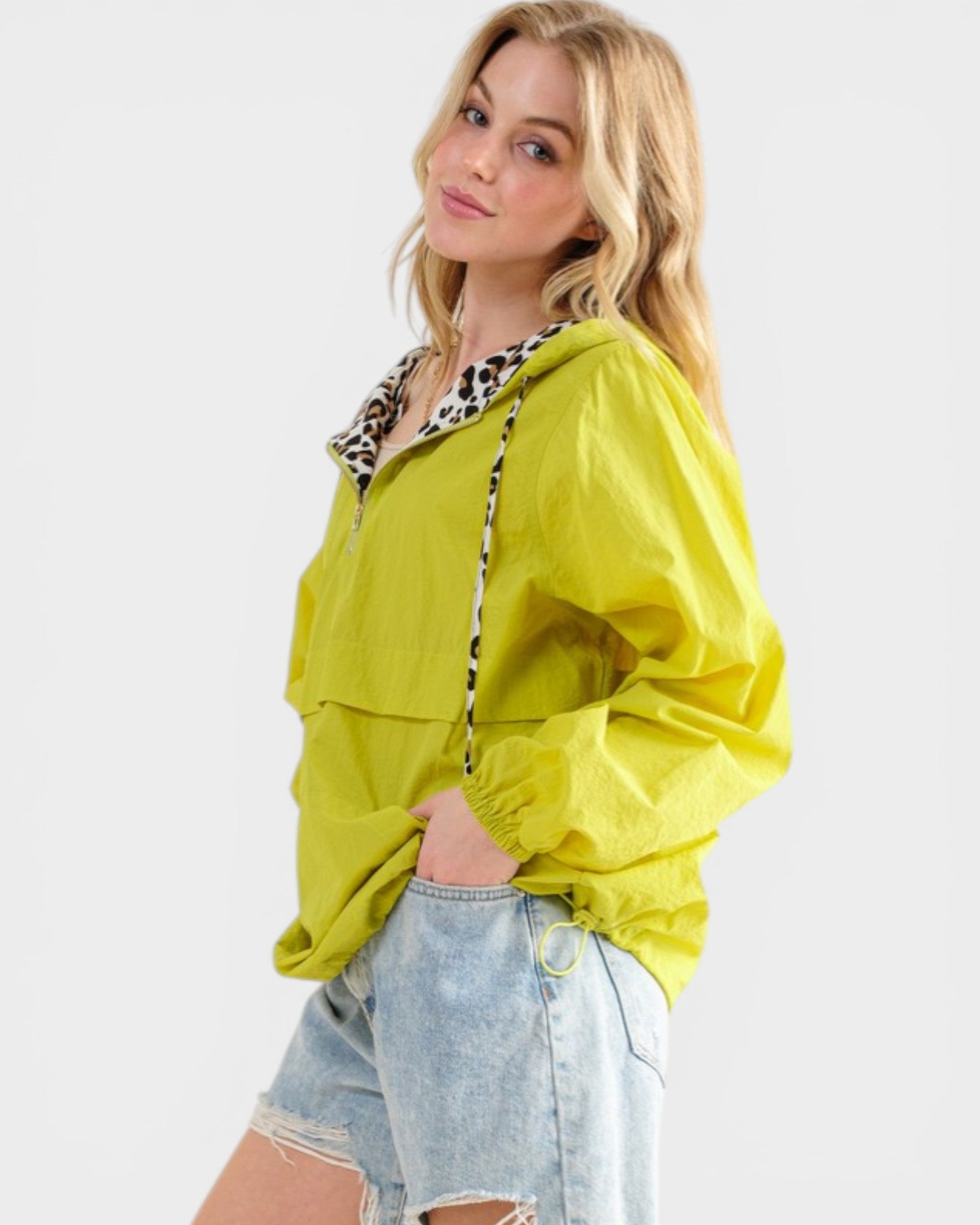 Woman wearing a bright yellow jacket with a leopard print trim on a white background