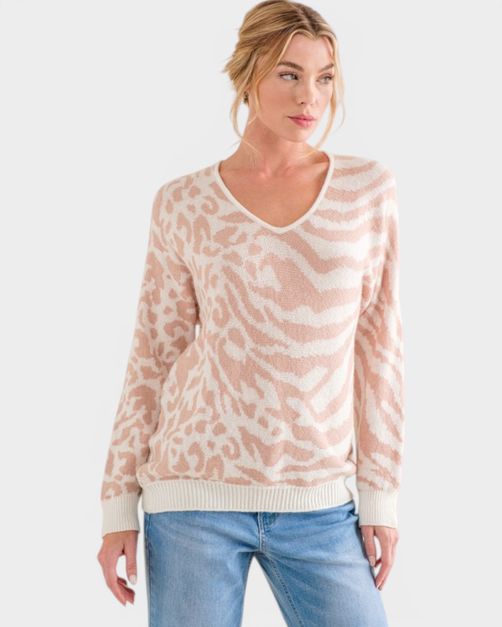 Woman wearing a light pink and white patterned sweater with blue jeans on a white background