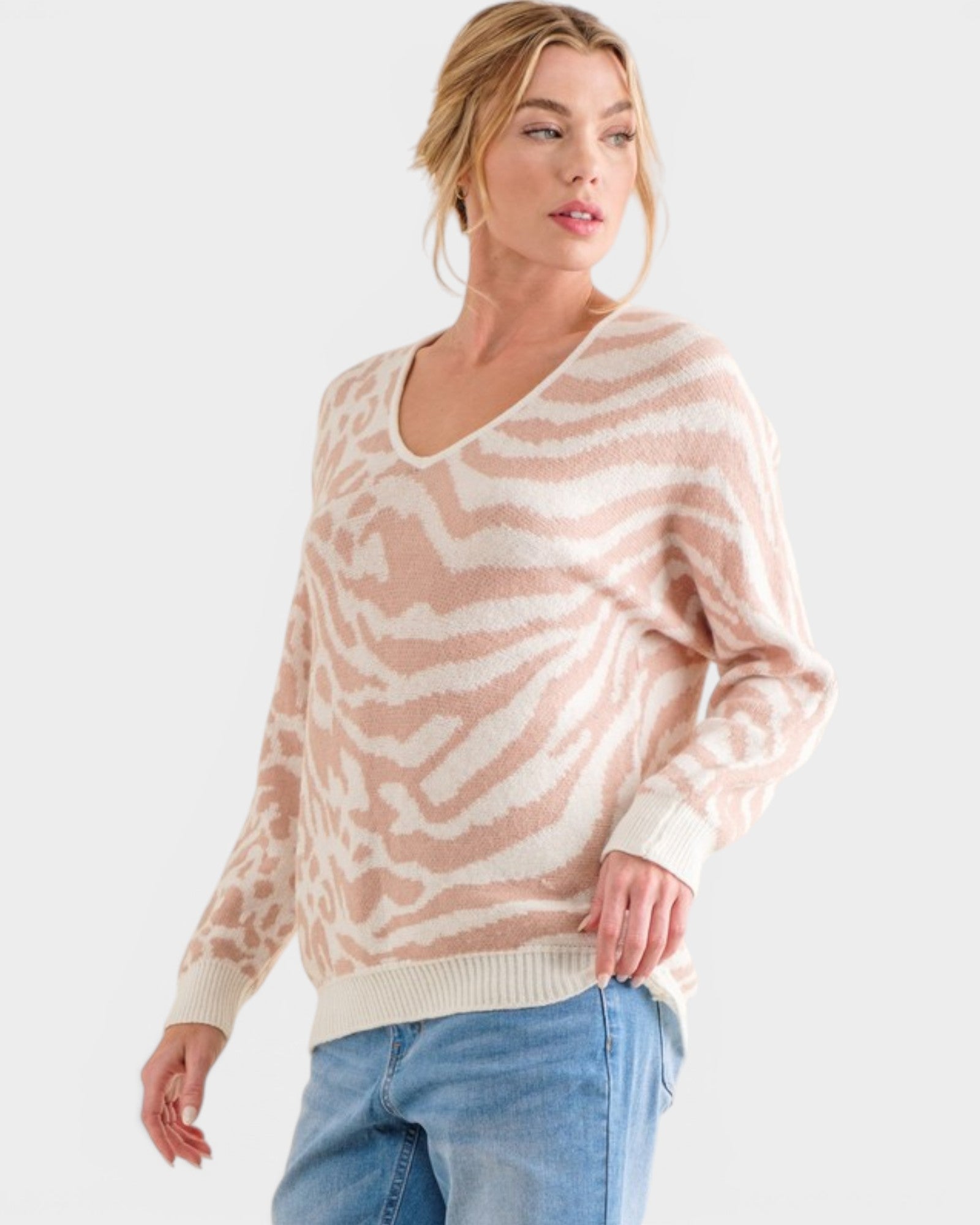 Woman wearing a beige and white patterned sweater with blue jeans on a white background